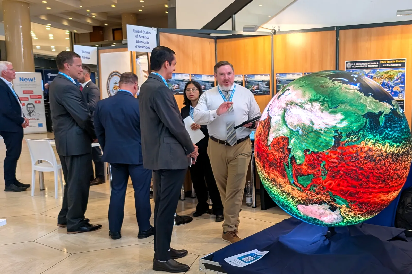 An Ayni LED sphere showing global ocean currents at the United States stand of the IHO Assembly, delegates talking beside it
