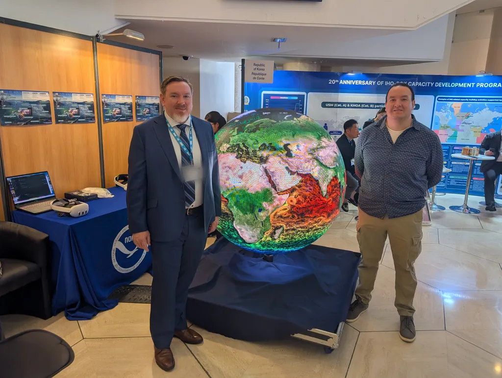 Two people standing either side of the Ayni sphere at the NOAA stand, the sphere showing ocean currents in vivid colour