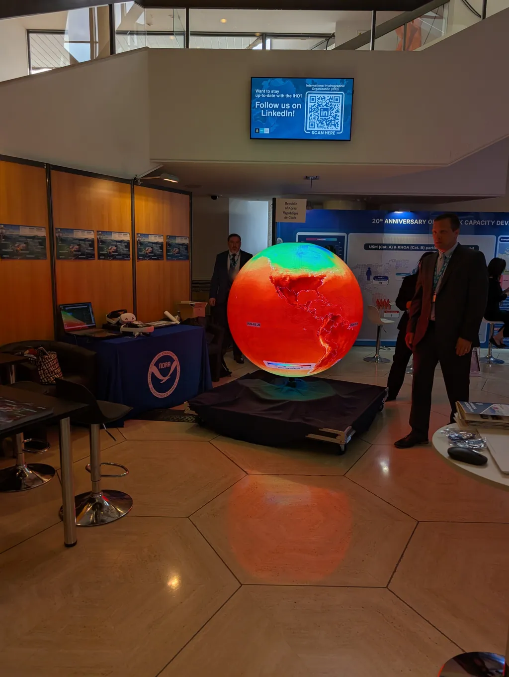 The Ayni sphere on its rolling case in an assembly hall, showing surface temperature beside the NOAA stand