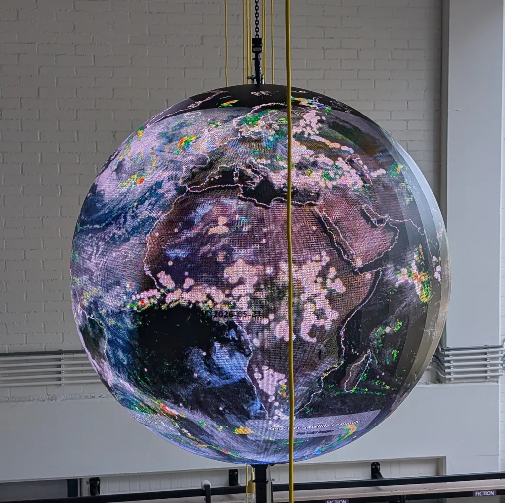A suspended Ayni sphere showing a global satellite composite above a school library