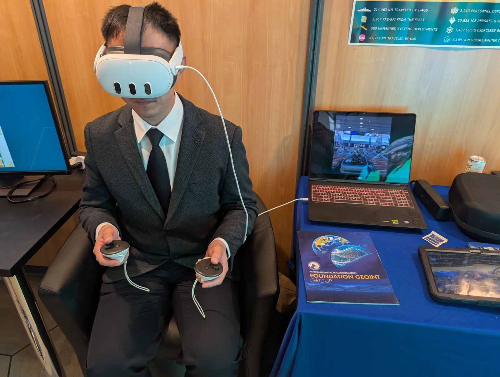 A seated delegate wearing a headset, with a laptop beside them mirroring what they see: the room itself, with a data globe placed in it
